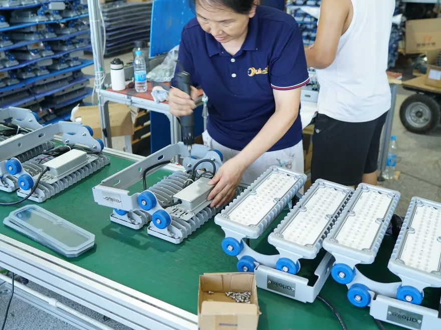 Assembly line workers installing LED boards, drivers, silicone gaskets and tempered glass into industrial luminaires