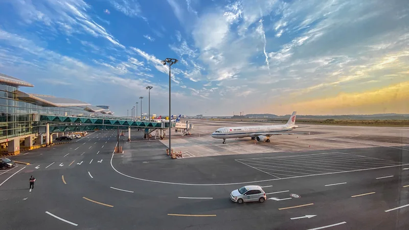 Airport apron at sunrise with an aircraft at the gate, lit by high mast lighting towers carrying rings of LED floodlights