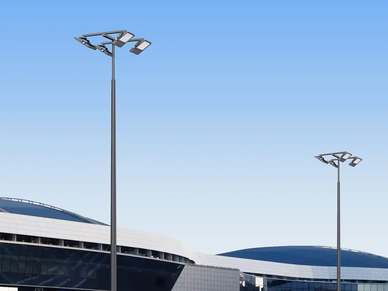 High mast lighting towers standing over the forecourt of an arena, each carrying a ring of aimed LED floodlights