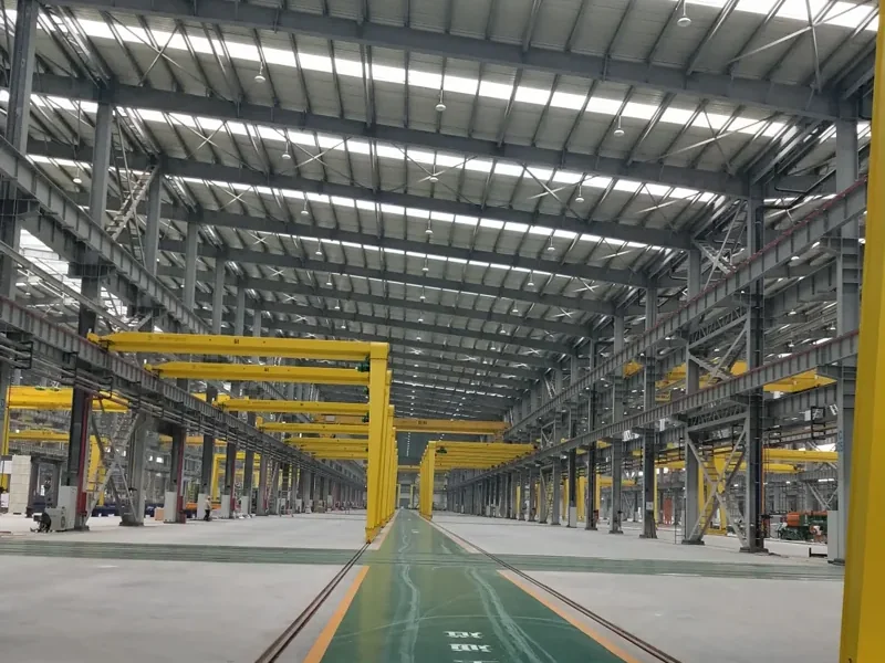 Factory production hall with overhead gantry cranes, lit end to end by LED high bay lights on the roof structure