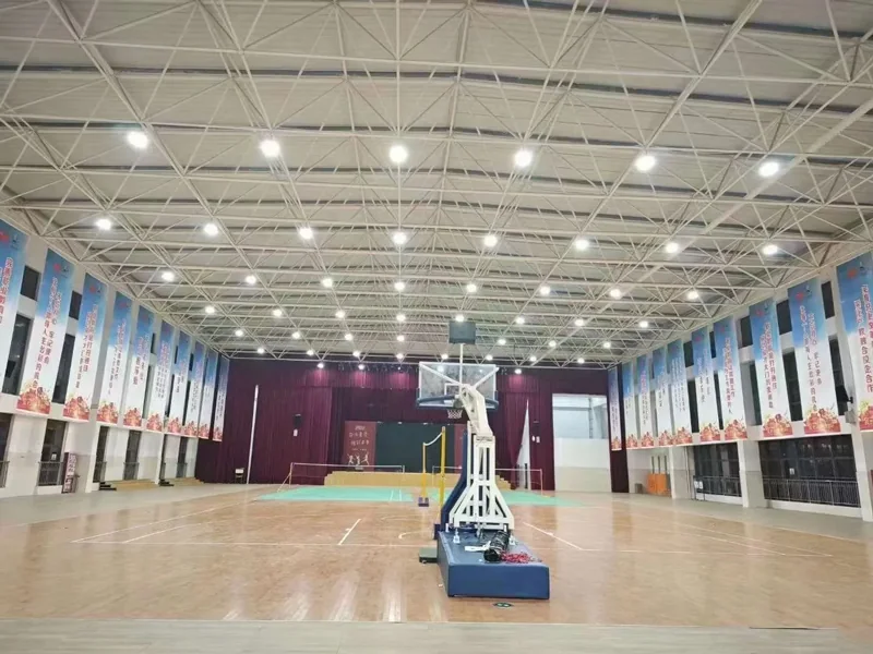 Indoor gymnasium with a basketball court lit by a grid of LED high bay fixtures mounted on the steel roof truss