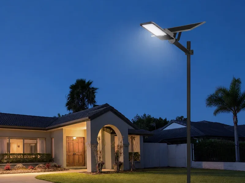 Solar street light on a pole outside a single-storey house at dusk, lighting the driveway with no mains connection