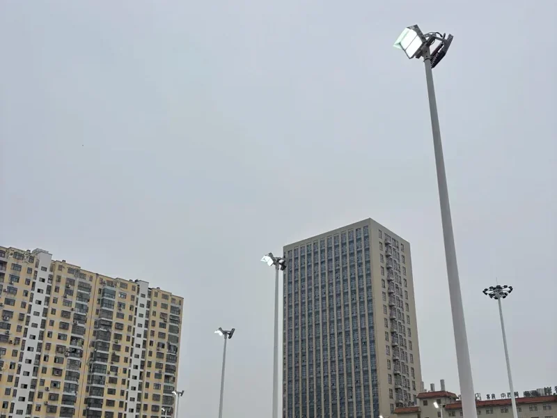 Outdoor sports court with slim floodlight masts along the sideline, lighting the playing surface from above