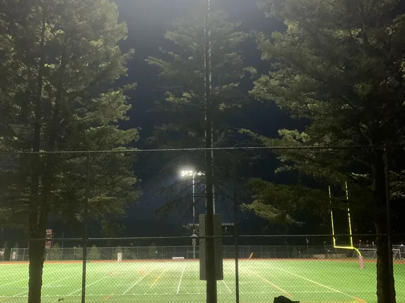 Sports field lit at night by mast-mounted LED floodlights, the pitch markings clearly visible across the playing surface