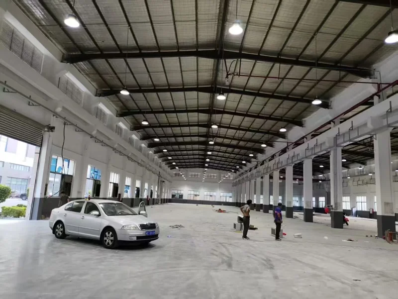 Wide warehouse hall lit by rows of LED high bay lights on the roof structure, with a vehicle parked on the open concrete floor